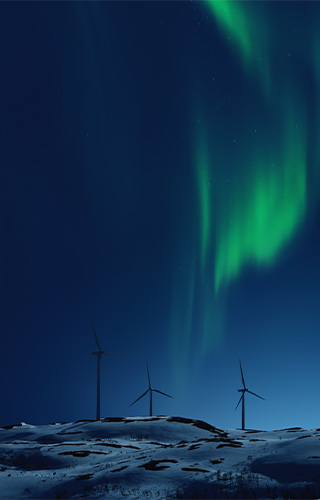 Wind turbines during winter night with a dark sky covered with green aurora.
